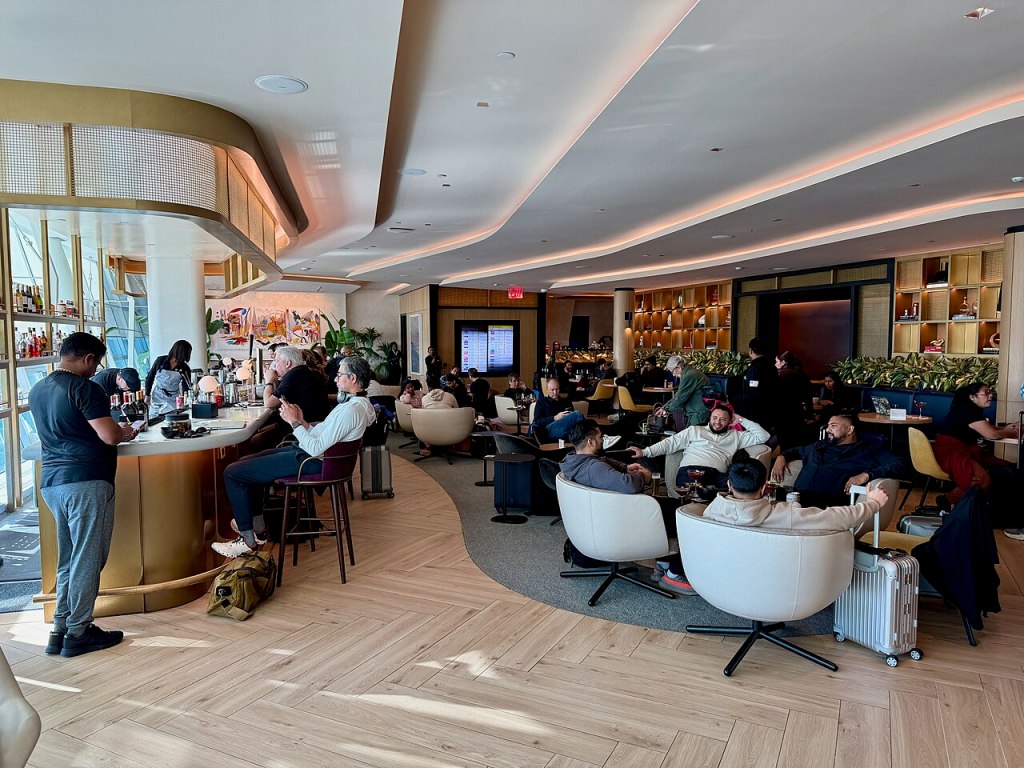 People sitting in chairs and at the bar in an airport lounge.