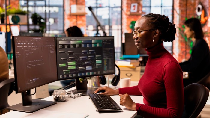Woman working on software development at a dual-screen workstation in a collaborative office space