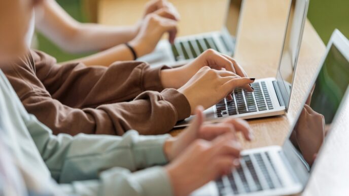 High school students sitting at the desk in the classroom during lesson, using laptops. Close up of hands, unrecognizable people.