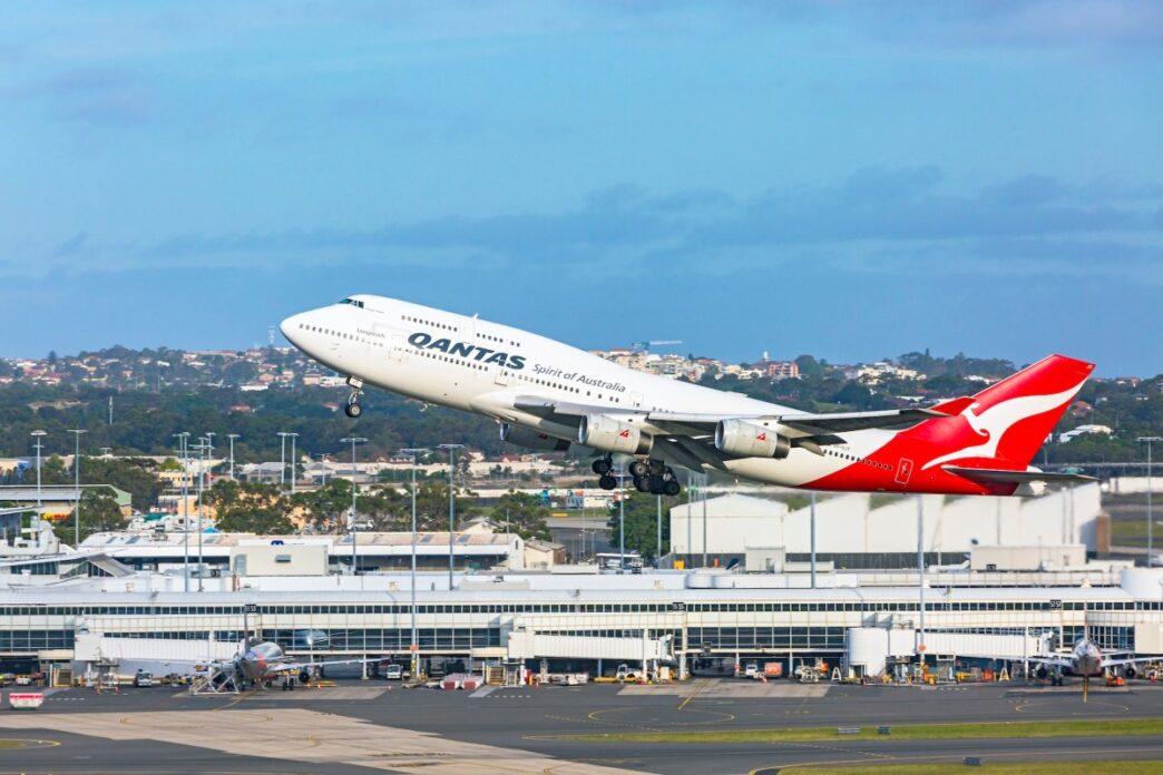 a Qantas 747 taking off from Sydney airport with the terminal building in the background.