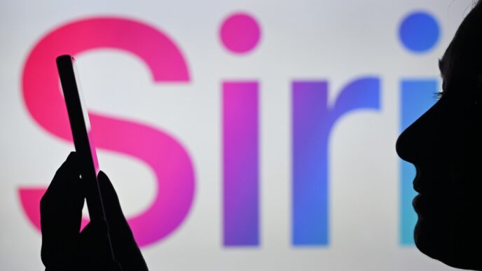 An image of a woman holding a cell phone in front of the Siri logo displayed on a computer screen.