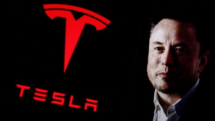 Elon Musk next to large red Tesla logo