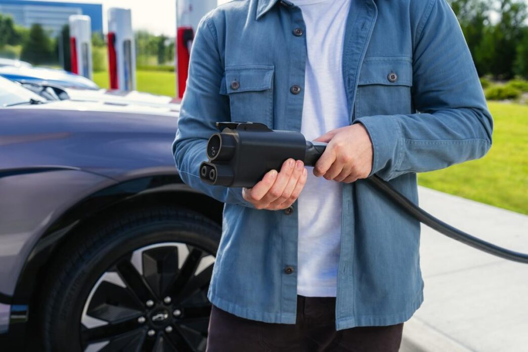 A man holds a Tesla charging cable with a CCS adapter attached.